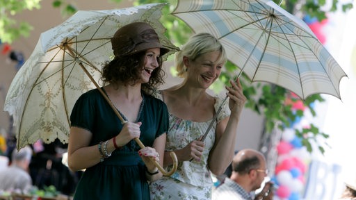 Zwei lachende Frauen in Sommerkleidern und mit Sonnenschirmen im Freien
