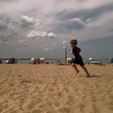 Ein kleiner Junge läuft an einem Strand entlang, im Hintergrund ist das Meer zu sehen und ein paar Strandkörbe.
