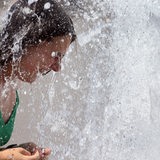 Eine junge Frau sucht bei sommerlicher Hitze Abkühlung in einem Citybrunnen