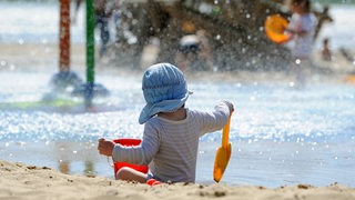 Ein kleiner Junge mit Sonnenmütze spielt bei schönstem Sommerwetter am Weserstrand von Bremerhaven (Bremen). 
