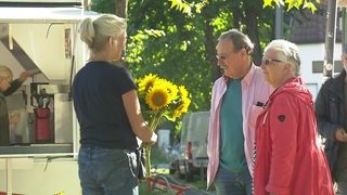 Eine Frau verkauft Sonnenblumen an ein Eghepaar