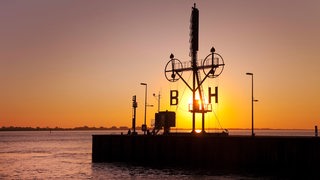 Die Sonne geht hinter einem Signalmast in Bremerhaven auf.