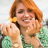 Eine Frau mit rötlichen Haaren und Sommersprossen cremt ihr Gesicht mit Sonnencreme ein.