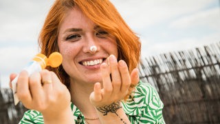 Eine Frau mit rötlichen Haaren und Sommersprossen cremt ihr Gesicht mit Sonnencreme ein.