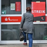Eine Frau steht vor der Tür der Sparkasse, an der ein Transparent mit der Aufschrift "Heute: Streik" hängt.