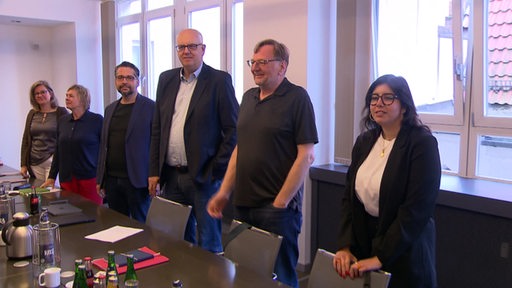 Mehrere Personen unter anderem der Bremer Bürgermeister Andreas Bovenschulte stehen hinter ihren Stühlen und lächeln.