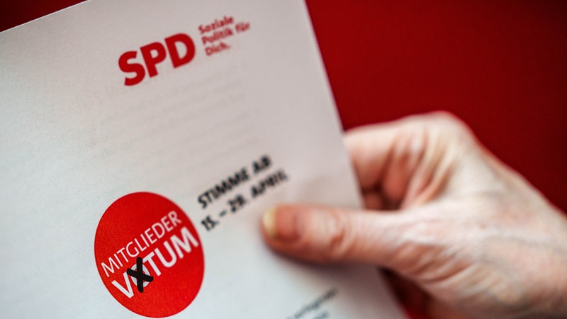 Eine Hand hält die Unterlagen, die SPD Mitgliedern zum Mitgliedervotum zum Koalitionsvertrag zugeschickt bekommen.