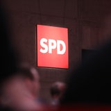 Leuchtenes SPD Logo, davor unscharf Menschen (Symbolbild)