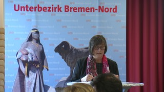An einem Rednerpult steht eine SPD Abgeordnete und im Hintergrund ist ein Plakat mit der Aufschrift "Unterbezirk Bremen-Nord" zu sehen.