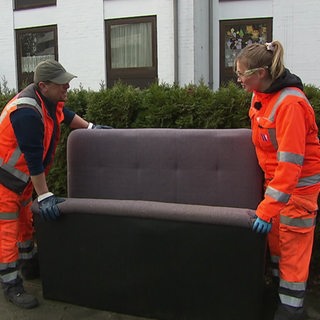Zwei Menschen tragen ein Sofa vom Straßenrand