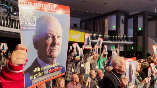 Protestplakate recken Gewerkschaftsmitglieder dem Kanzler während seiner Rede im Bremer Kongresszentrum entgegen.