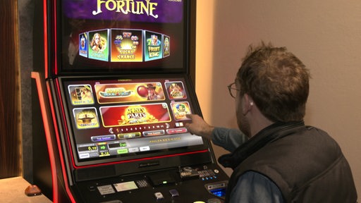 Ein Mann sitzt in einer Spielhalle an einem Spielautomat.