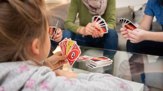 Eine Familie spielt gemeinsam ein Kartenspiel im Wohnzimmer (Symbolbild)