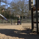 Ein Jugendlicher im Rollstuhl ist zwischen Spielgeräten auf einem Spielplatz zu sehen.