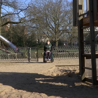 Ein Jugendlicher im Rollstuhl ist zwischen Spielgeräten auf einem Spielplatz zu sehen.