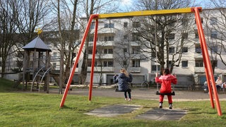 Zwei Kinder sitzen auf Schaukeln auf einem Spielplatz.