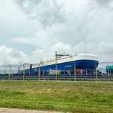 Hinter einem Zaun liegt ein großes blaues Frachtschiff.