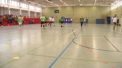 Mehrere Personen spielen in einer Sporthalle gemeinsam Fußball.