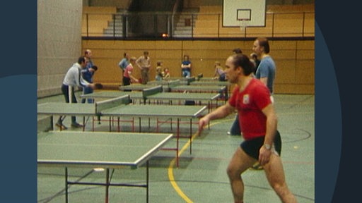 Mehrere Personen spielen in einer Sporthalle Tischtennis.