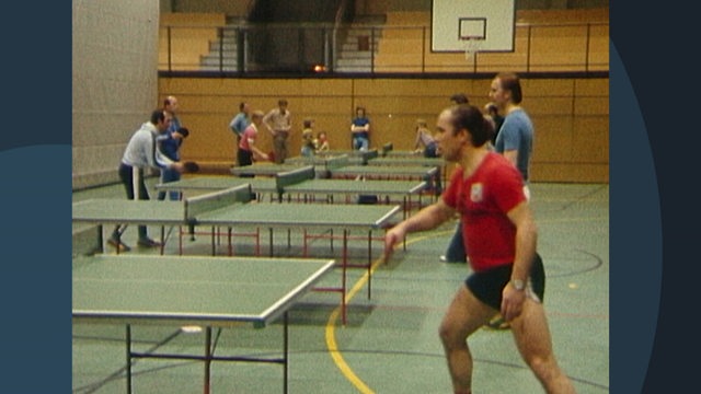 Mehrere Personen spielen in einer Sporthalle Tischtennis.