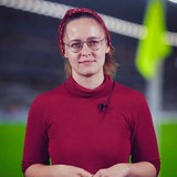 Eine Reporterin steht vor dem Foto eines Fußballtors.