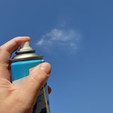 Eine Hand hält eine Sprühdose und drückt auf den Sprühkopf