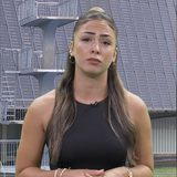 Eine Moderatorin steht vor dem Bild eines Sprungturms.