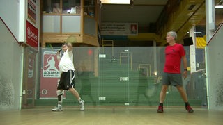 Zwei Herren spielen Squash gegeneinander in einer Halle