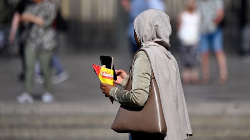 Eine schwarze Frau mit Kopftuch schaut auf ihr Handy.