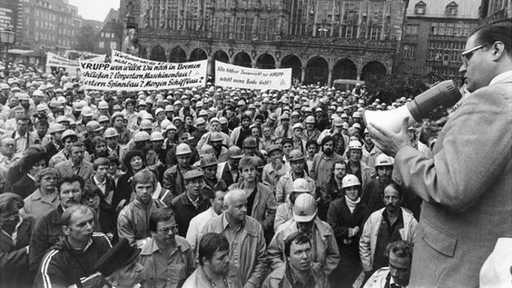 Der damalige Bürgermeister von Bremen Hans Koschnik spricht per Megafon mit den demonstrierenden Beschäftigten der AG Weser 1983 auf dem Bremer Marktplatz