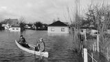 Zwei Männer paddeln durch ein überschwemmtes Kleingartengebiet