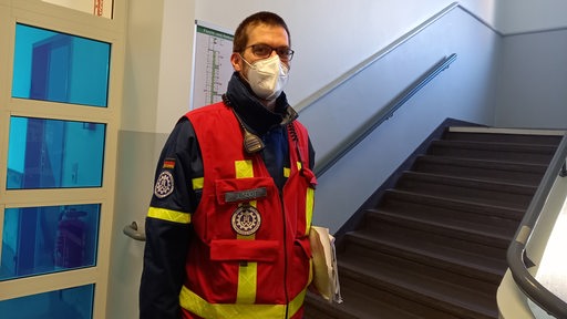 Ein Mann mit Maske und Rettungsuniform steht in einem Treppenhaus.