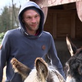 Ein Mann mit Kapuze steht in einem Esel-Gehege.