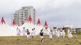 Eine Gruppe von Kindern rennt Richtung Kamera hinter ihnen ein Zelt und ein Hochhaus