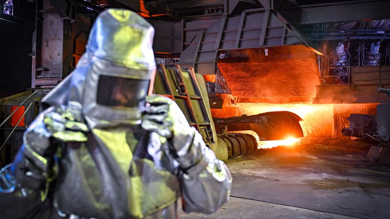Ein Mitarbeiter in Schutzkleidung steht beim Abstich von Roheisen an einem Hochofen