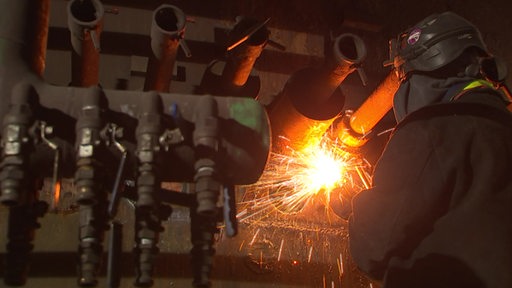 Ein Angestellter im Stahlwerk schweißt unter Funken Rohre.