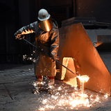 Ein Arbeiter in einem Stahlwerk nimmt an einem Hochofen eine Probe des flüssigen Roheisens. 