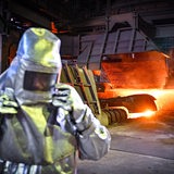 Ein Mitarbeiter in Schutzkleidung steht beim Abstich von Roheisen an einem Hochofen 