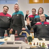 Mehrere Personen in Uniformen grüßen per Handzeichen in die Kamera.