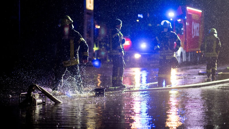 Einsatzkräfte der Feuerwehr pumpen das Wasser vom Hof einer Autowerkstatt ab.