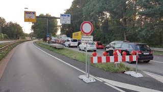 Ein Baustellenschild steht auf einer Straße, auf der danebenliegenden Spur, stehen Autos im Stau.