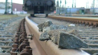 Steine liegen auf einem Gleis und eine Bahn naht heran