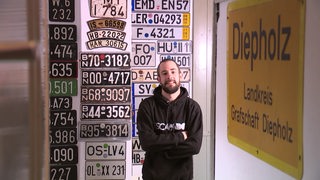 Der Sammler von Autokennzeichen Stephan Lück steht vor einer Wand voller Kennzeichen in seinem Zuhause.