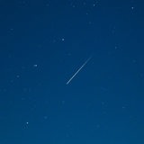 Eine Sternschnuppe leuchtet am Sternenhimmel.