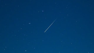 Eine Sternschnuppe leuchtet am Sternenhimmel.