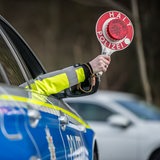 Eine Hand hält eine Polizeikelle mit der Aufschrift "Halt-Polizei" aus dem Fenster.