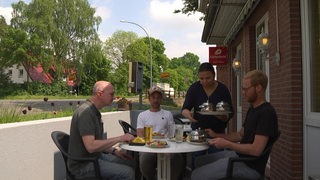 Drei Männer sitzen in einem Bistro und essen zu Mittag. 