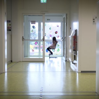 Ein Mädchen sitzt alleine auf einem Schulflur.