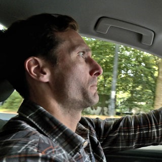 Ein Mann hinterm Steuer macht ein erschrockenes Gesicht.