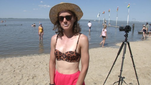 Eine junge Frau mit Sonnenbrille und Strohhut gibt in Dangast am Strand ein Interview. 